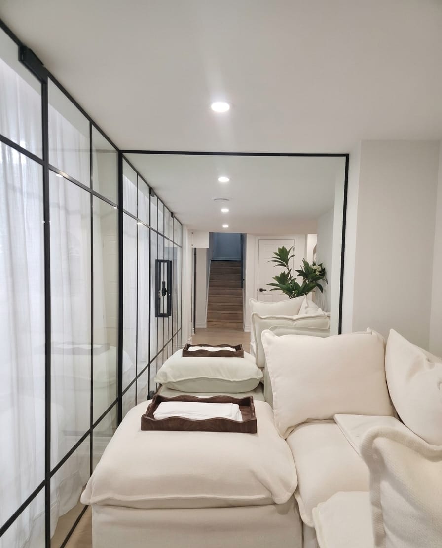 Black-frame floor-to-ceiling glass partition wall enclosing residential lounge with cream sectional sofa and sheer curtains — Built By Glass, GTA