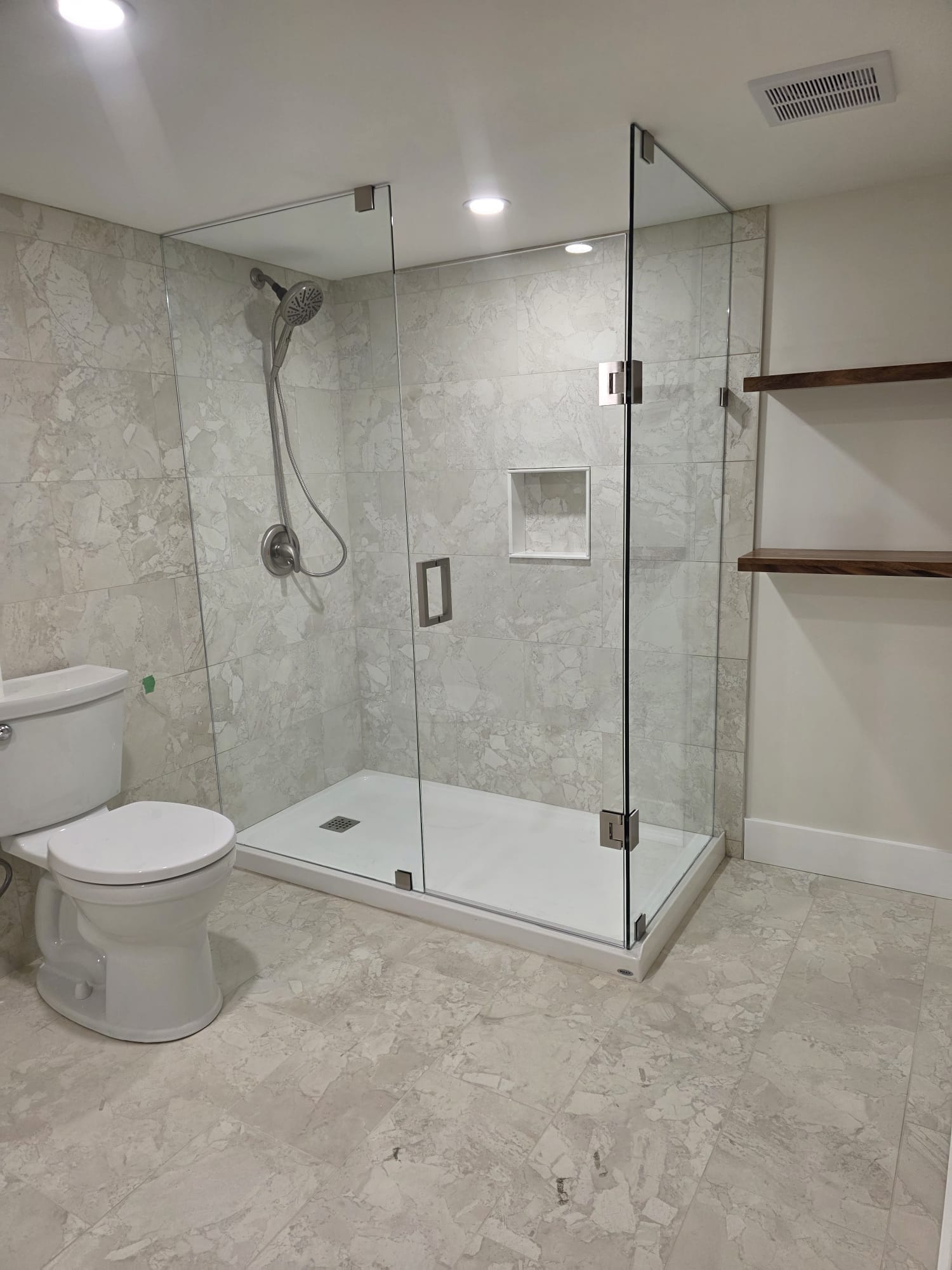 Frameless corner glass shower enclosure on Carrara marble tile with brushed nickel rain head and recessed niche — Built By Glass, basement bathroom