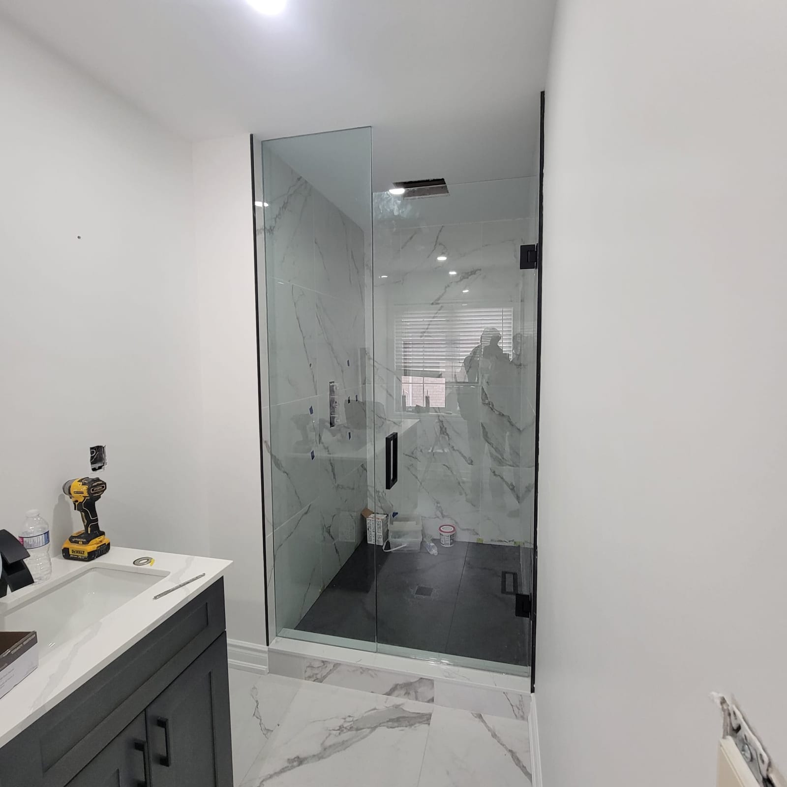Frameless glass shower enclosure with black hardware and marble walls — Built By Glass