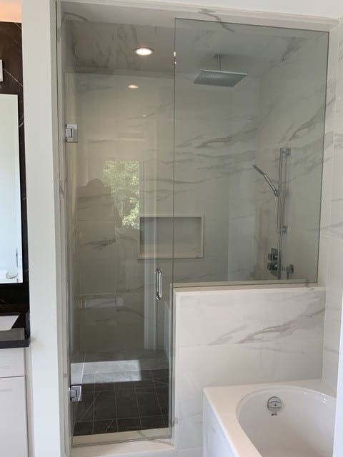 Frameless glass shower with marble tile and built-in niche beside a soaker tub — Built By Glass