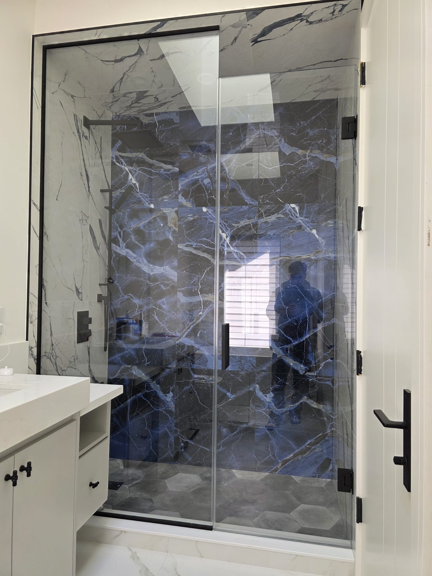Frameless sliding glass shower door with dramatic blue exotic marble feature wall and hexagon tile floor — Built By Glass, GTA
