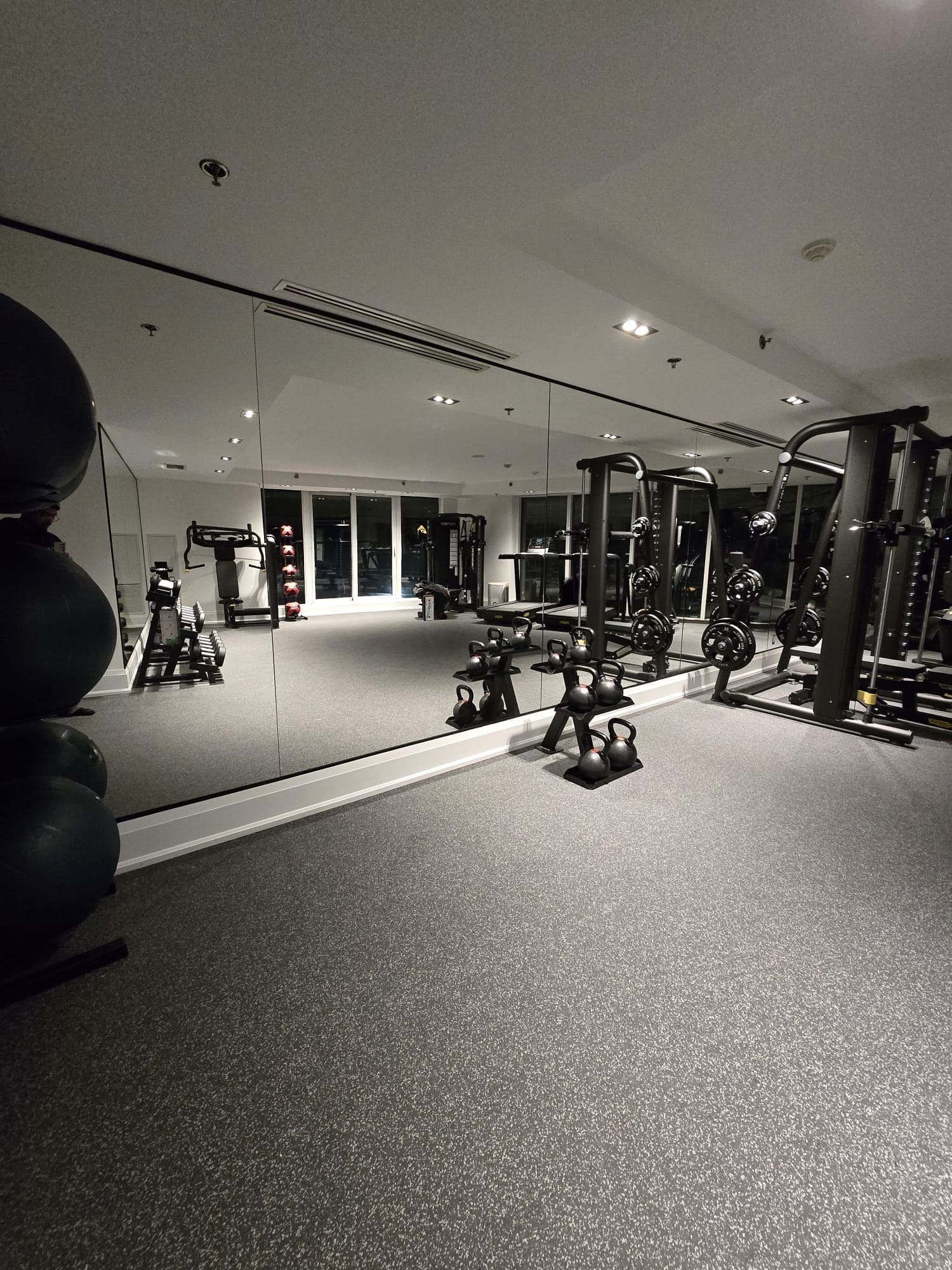 Floor-to-ceiling frameless home gym mirror wall reflecting full weight rack, dumbbells and recessed pot lighting — Built By Glass, GTA