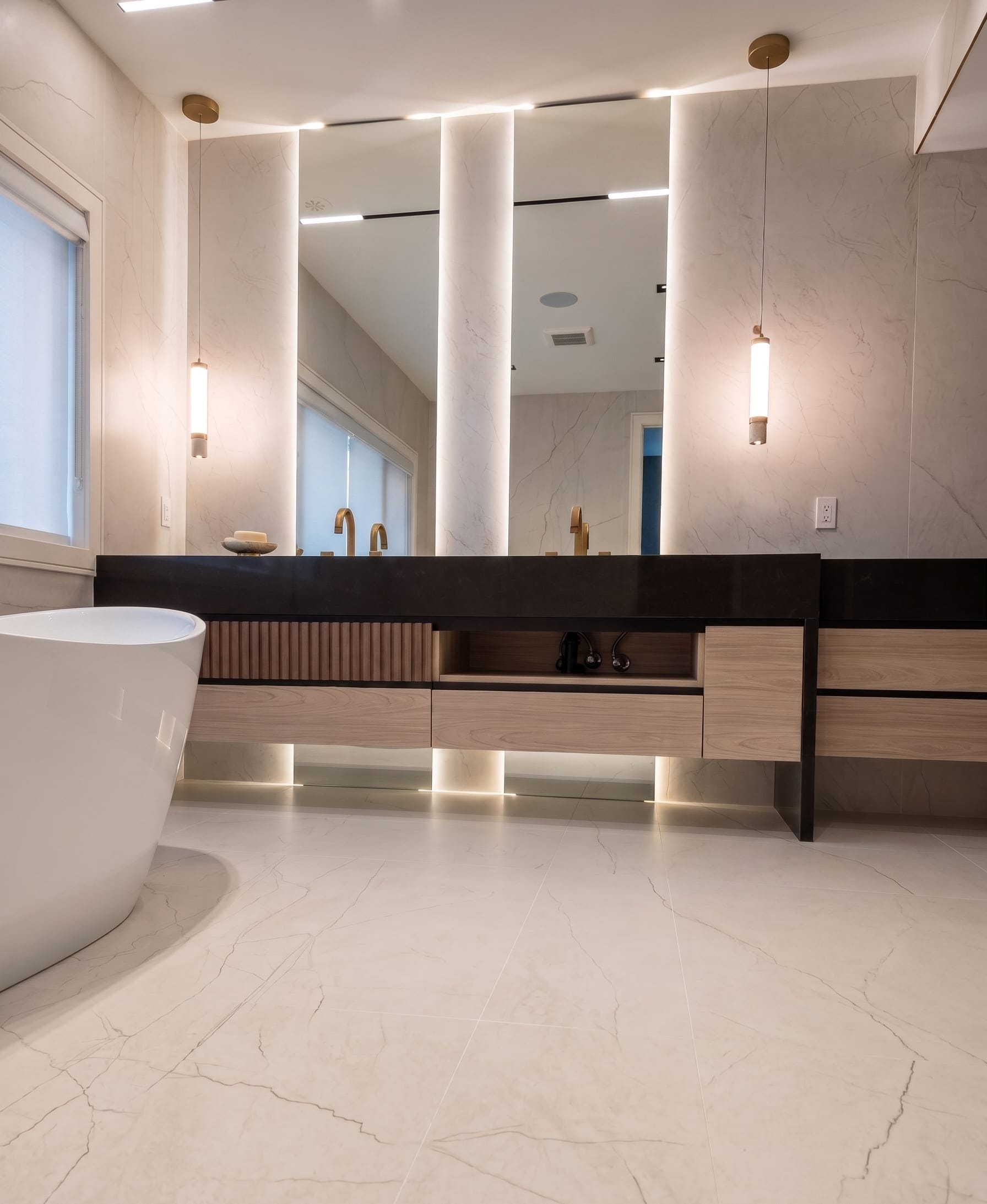 Custom wall-to-wall LED backlit master bathroom mirror with brass pendant lighting, freestanding tub, fluted wood vanity and Calacatta marble walls — Built By Glass, GTA