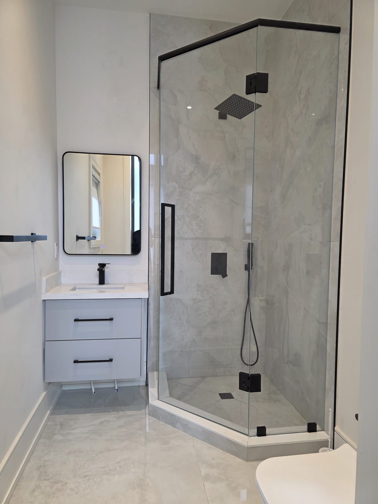 Neo-angle frameless glass shower with matte black hardware, rain shower head and grey marble tile — Built By Glass, GTA