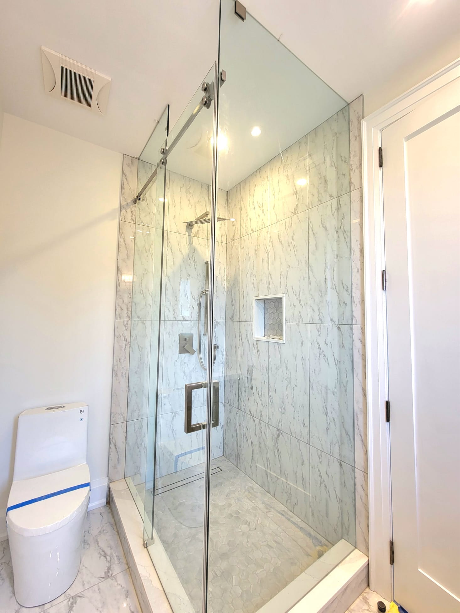 Sliding glass shower door on a marble-tiled enclosure — Built By Glass